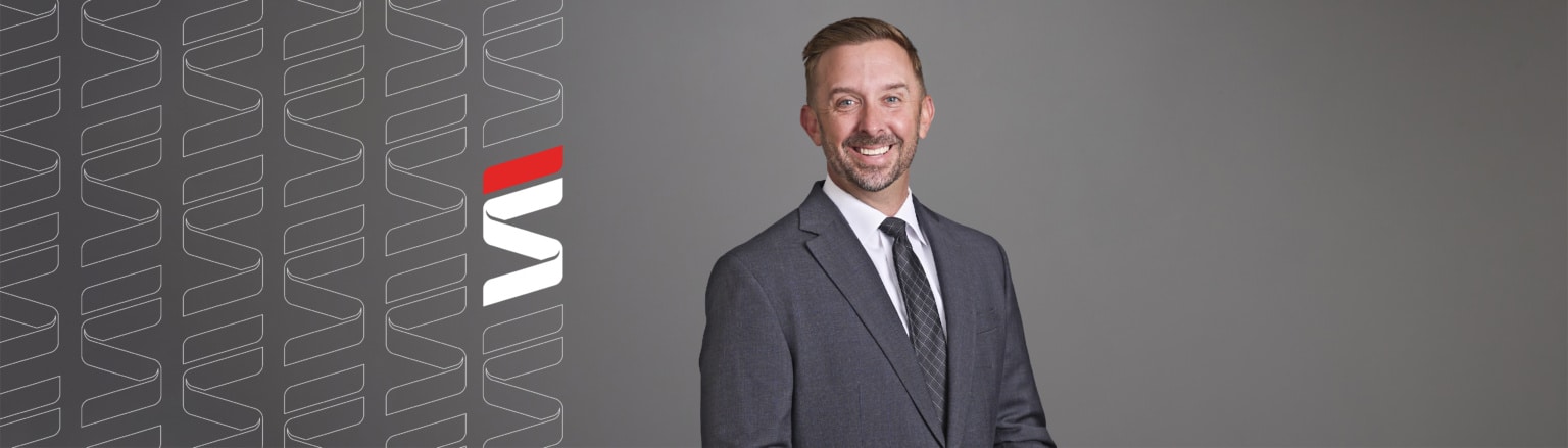 Eric Wells, Fraser Stryker attorney, wearing a grey suit jacket, white shirt and grey striped tie. Fraser Stryker logo icon repeating on the left side of the photo.